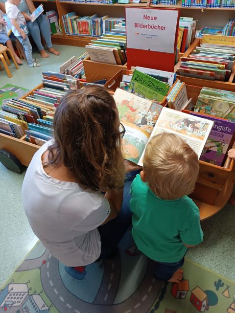 Mutter mit Kleinkind beim Vorlesen vor der Bücherkiste
