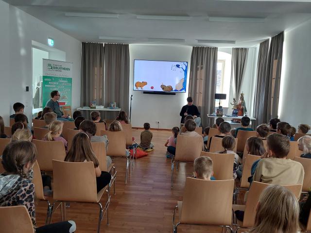 Kinder sitzen im Pfarrhof und lauschen der Lesung von Matthäus Bär